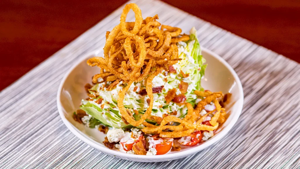 Wedge salad with creamy dressing, bacon, blue cheese, tomatoes, crispy onions.