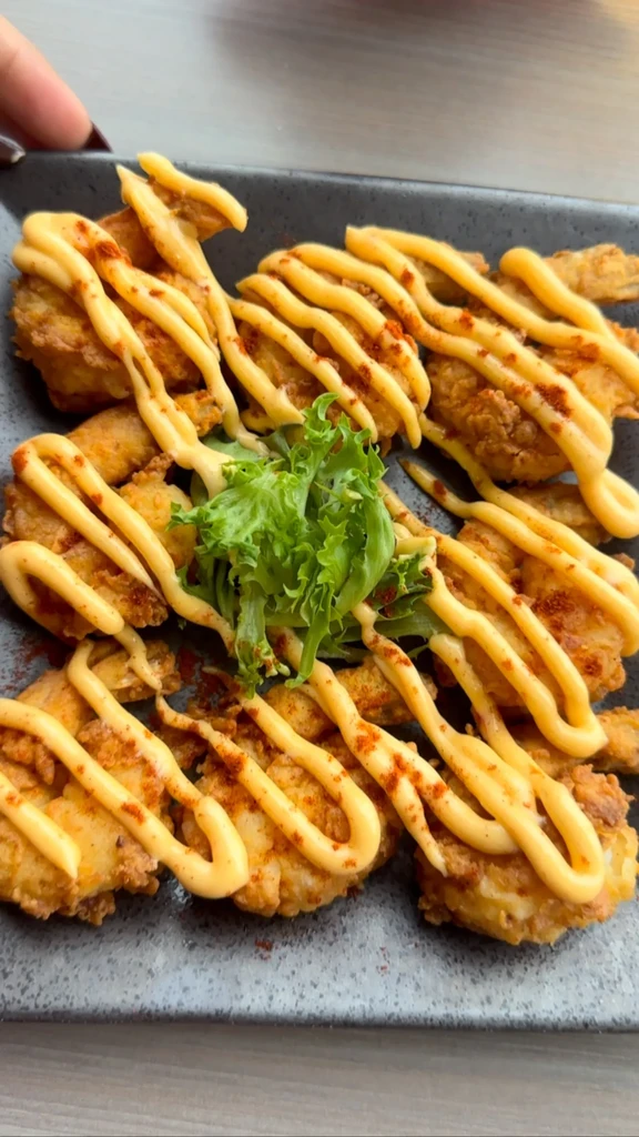 Crispy fried pieces drizzled with sauce, topped with spice and green lettuce.