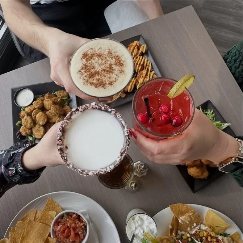 Overhead view of hands toasting diverse cocktails and appetizers.