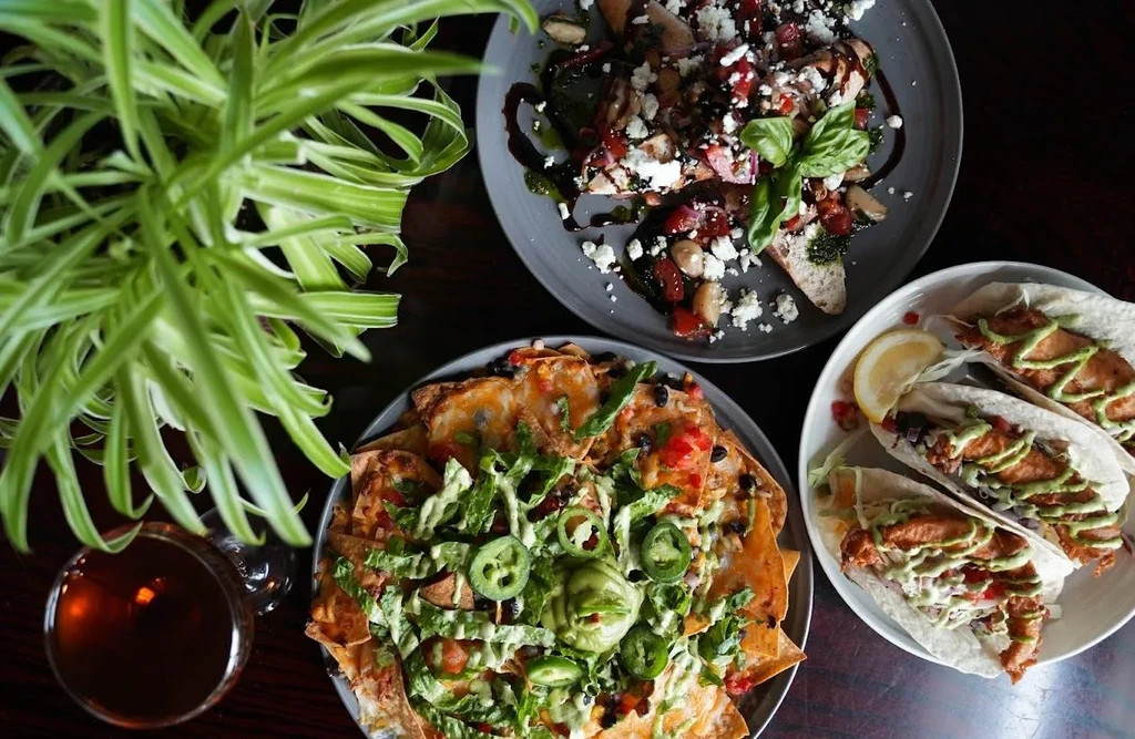 Overhead of nachos, bruschetta, tacos, and a drink on a wooden table.