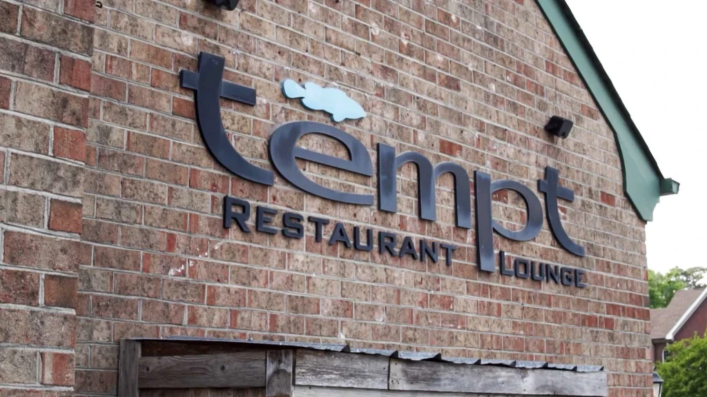 Exterior brick wall with 'tempt RESTAURANT LOUNGE' sign and blue fish.