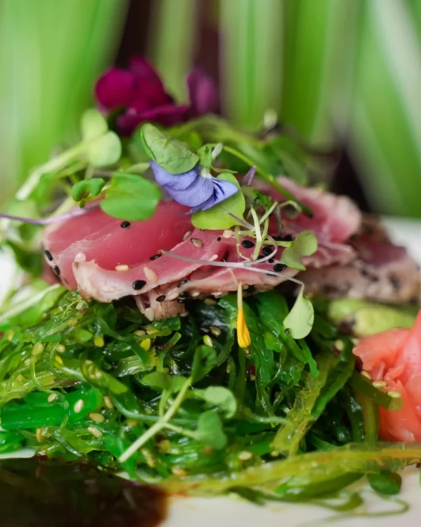 Seared tuna tataki, seaweed salad, pickled ginger, garnished with flowers.