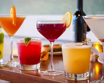 Five diverse cocktails with garnishes on a wooden bar top.