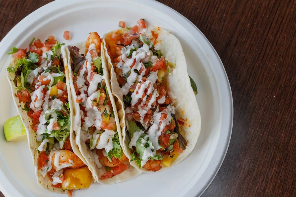 Three shrimp tacos with mango, tomato, lettuce, and a lime wedge.