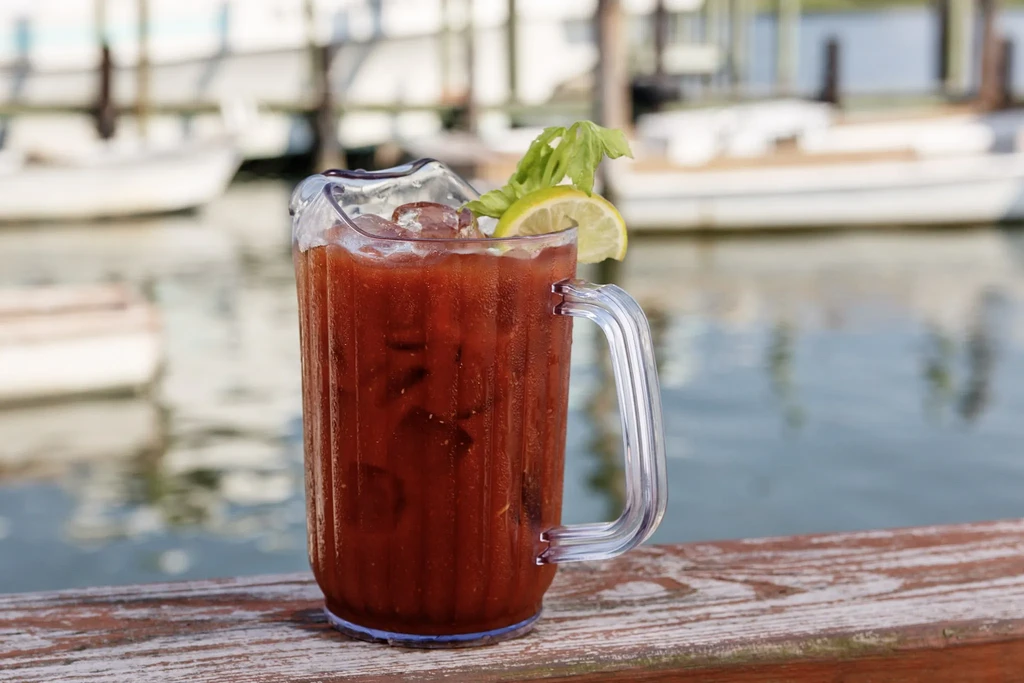 Large plastic Bloody Mary pitcher with lime, celery, near boats.