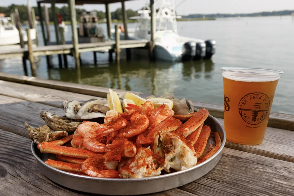 Platter of Old Bay shrimp, crab, oysters, and beer on a deck.