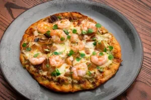 Flatbread with shrimp, melted white cheese, mushrooms, and green sprouts.