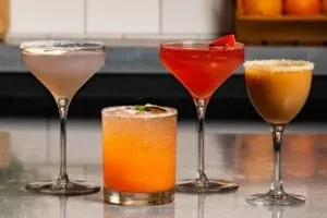 Four unique, colorful cocktails with garnishes on a reflective bar.