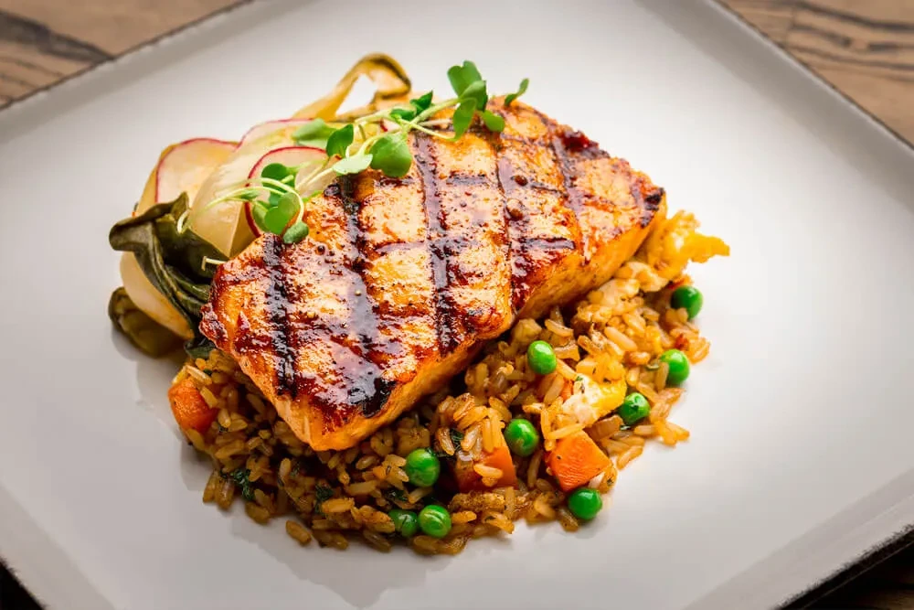 Grilled salmon, brown rice, peas, carrots, and greens on a modern plate.