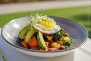 Fried egg, avocado, and sprouts atop colorful potato hash.