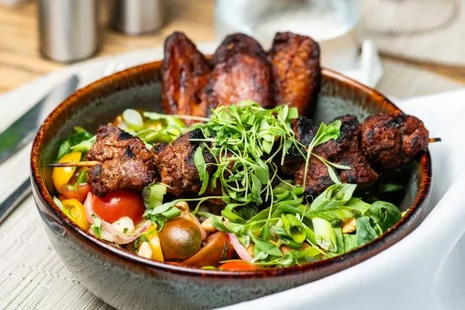 Bowl of grilled meat kebabs and fresh salad garnished with microgreens.