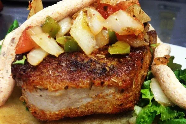 Pan-seared meat with golden crust, sautéed vegetables, lettuce, and breadsticks.