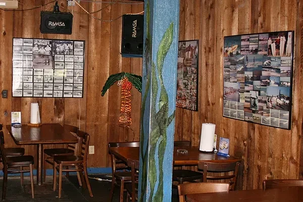 Rustic restaurant interior with wood panels, blue column, and beach photo collages.