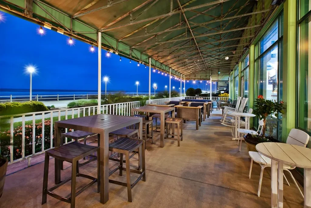 Twilight restaurant patio with diverse seating, string lights, and ocean view.