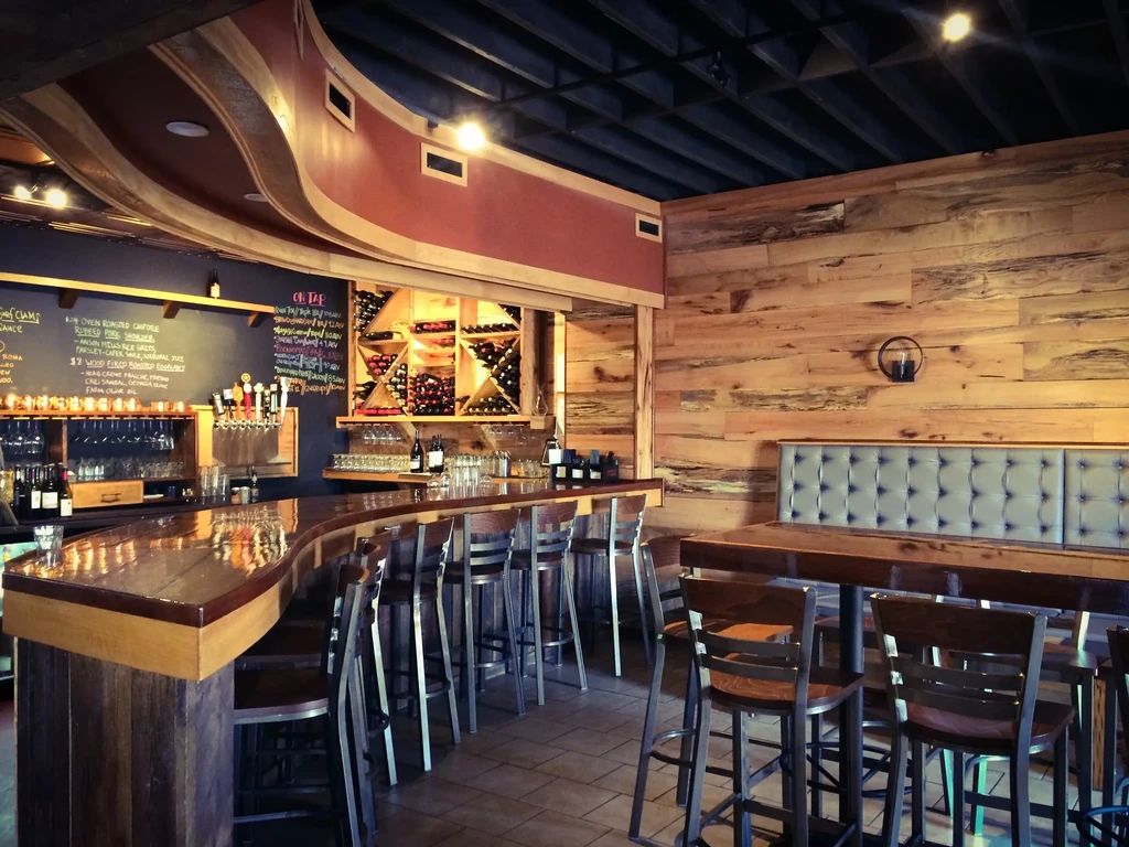 Modern rustic restaurant interior with curved wooden bar and chalkboard menu.
