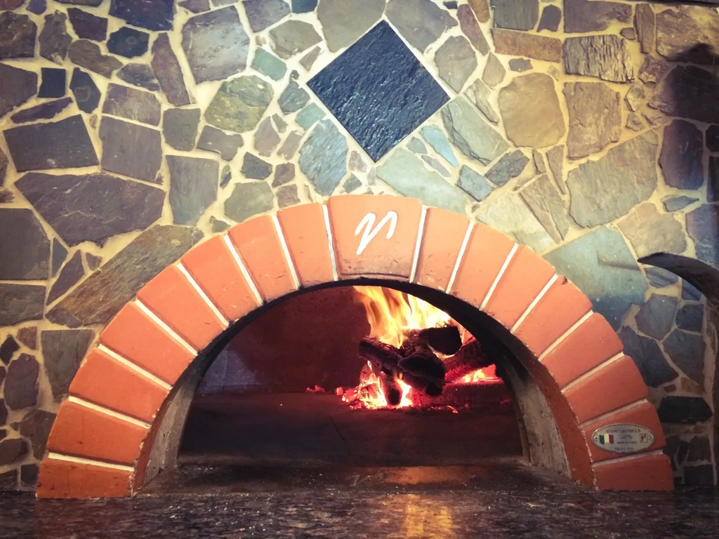 Traditional wood-fired oven with arched bricks, mosaic facade, and fire.