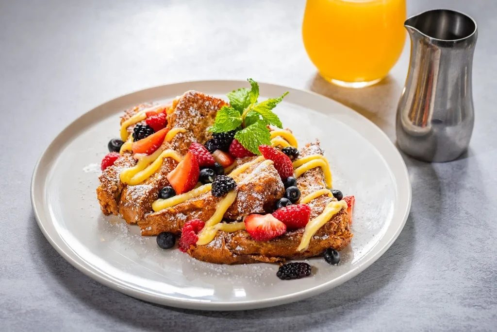 Golden toast with fresh berries, yellow sauce, powdered sugar, and mint.