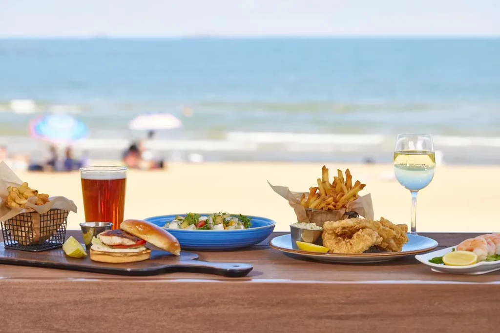 Beachfront dining: seafood, fries, salad, beer, and wine on a table.