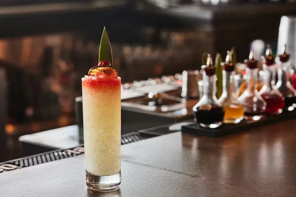 Vibrant layered cocktail with red ice, citrus and cherry on bar.