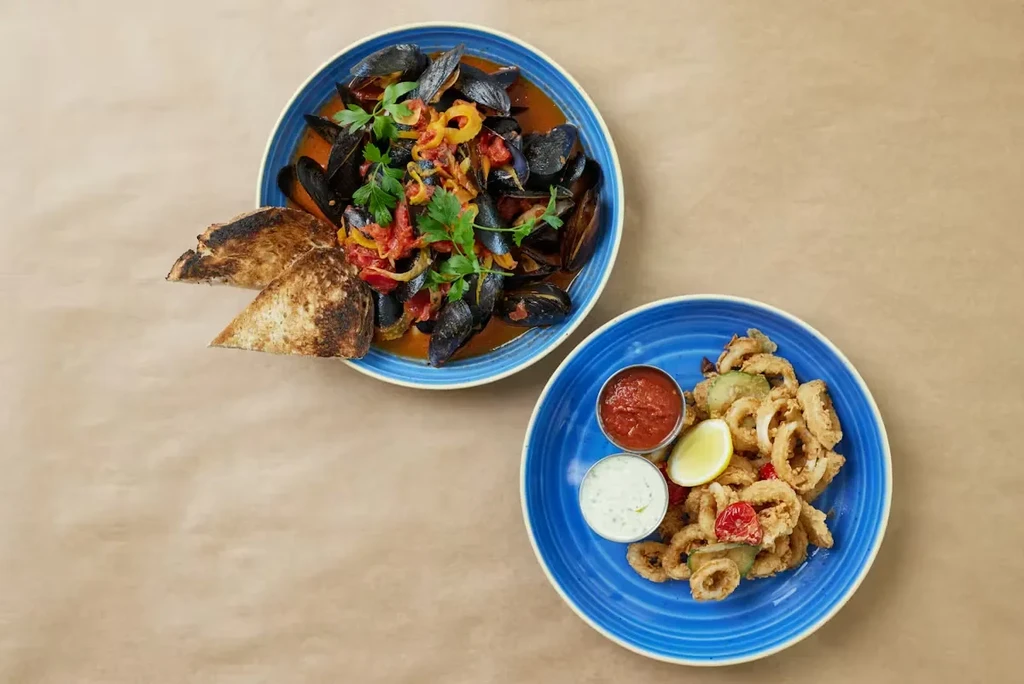 Steamed mussels and fried calamari, with bread and dips, on blue plates.