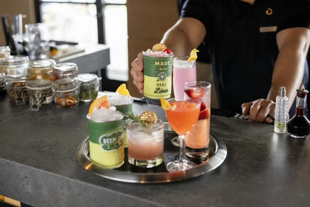 Five garnished cocktails on a silver tray held by a bartender.