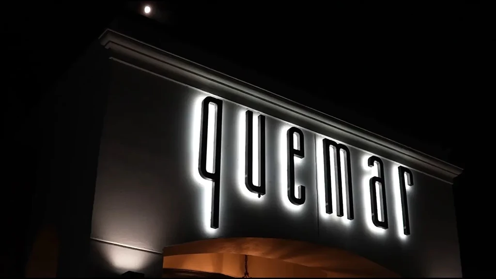 Illuminated "quemar" sign with glowing white halo effect at night.