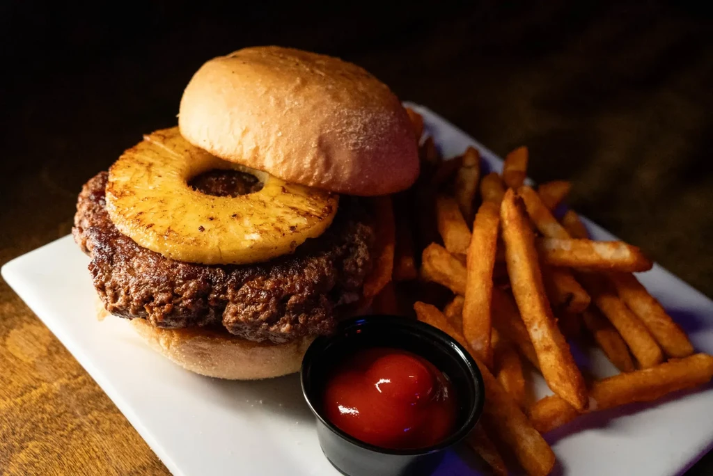 Gourmet burger with pineapple, golden fries, and ketchup.
