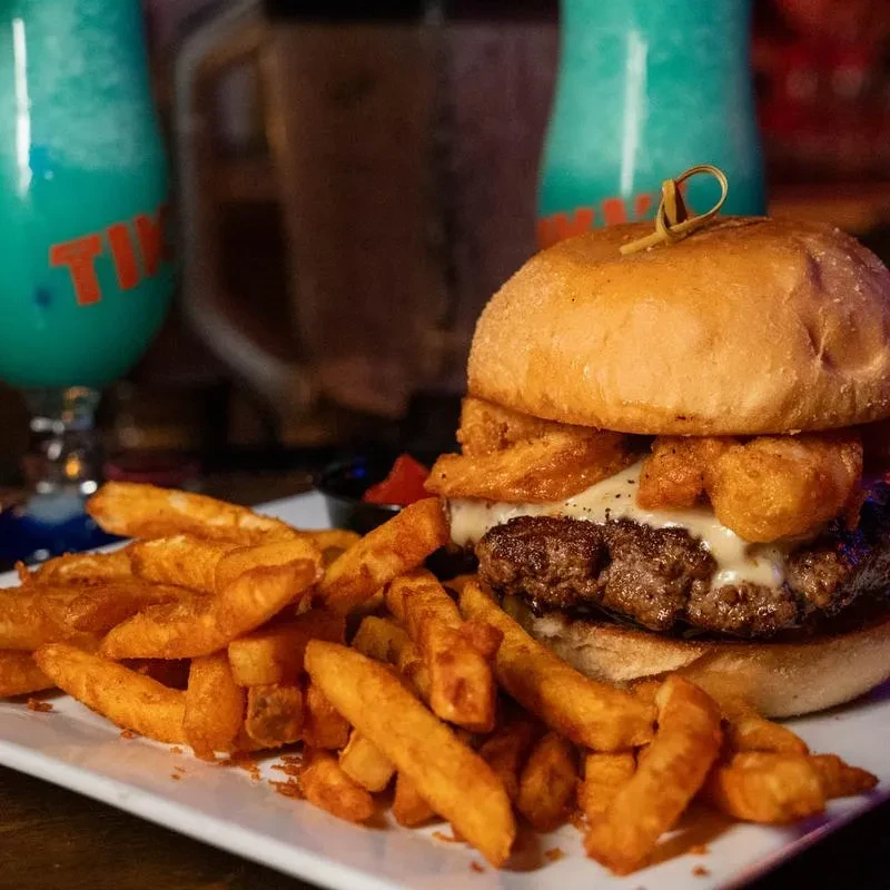 Juicy burger with melted cheese, fried toppings, and crispy fries on a plate.
