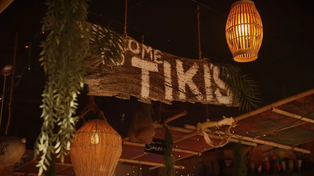 Tiki bar interior with "OME TIKI" sign, warm lanterns, tropical decor.