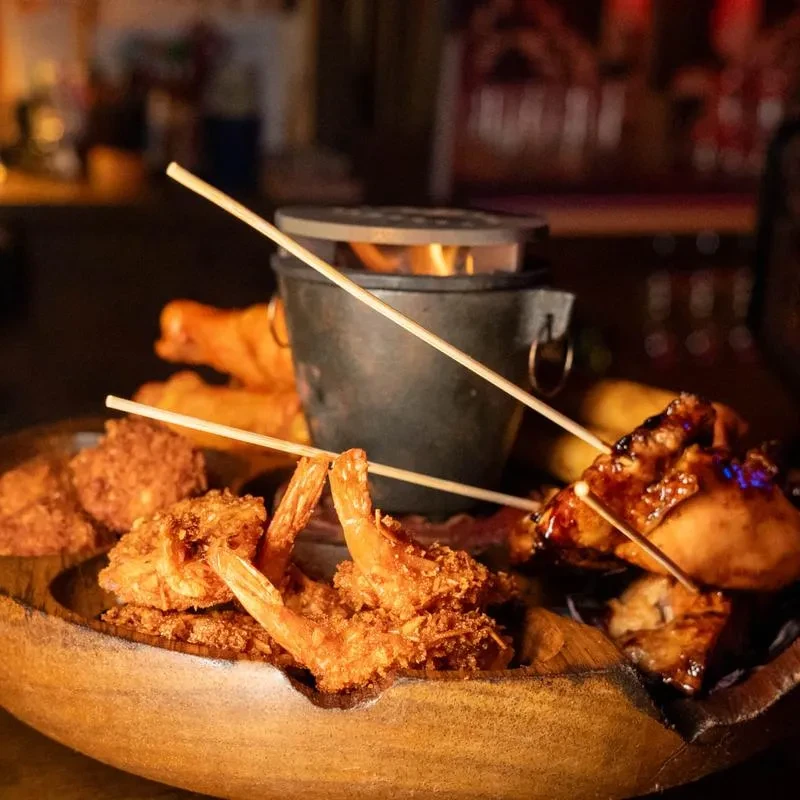 Rustic platter with fried shrimp, chicken skewers, and a warming flame.
