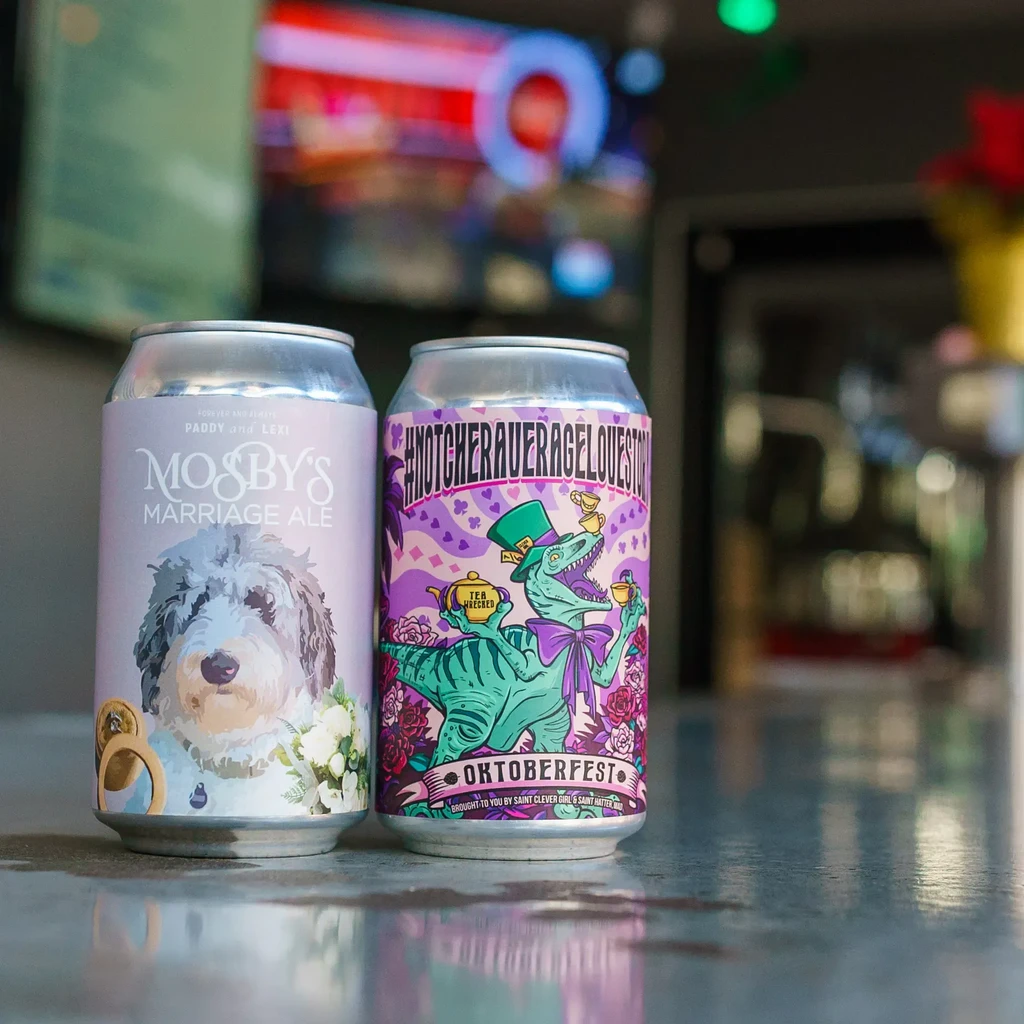 Two beverage cans: purple dog label, multi-colored dinosaur label.