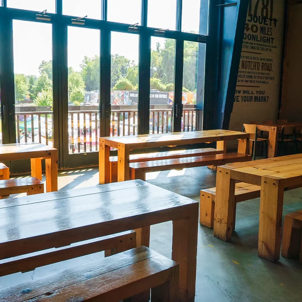 Industrial restaurant interior: long wooden tables, concrete floor, glass wall.