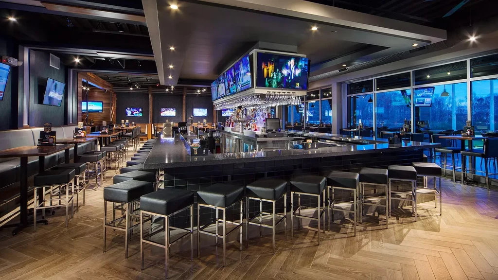 Modern bar and restaurant interior, long bar, multiple TVs, no people.
