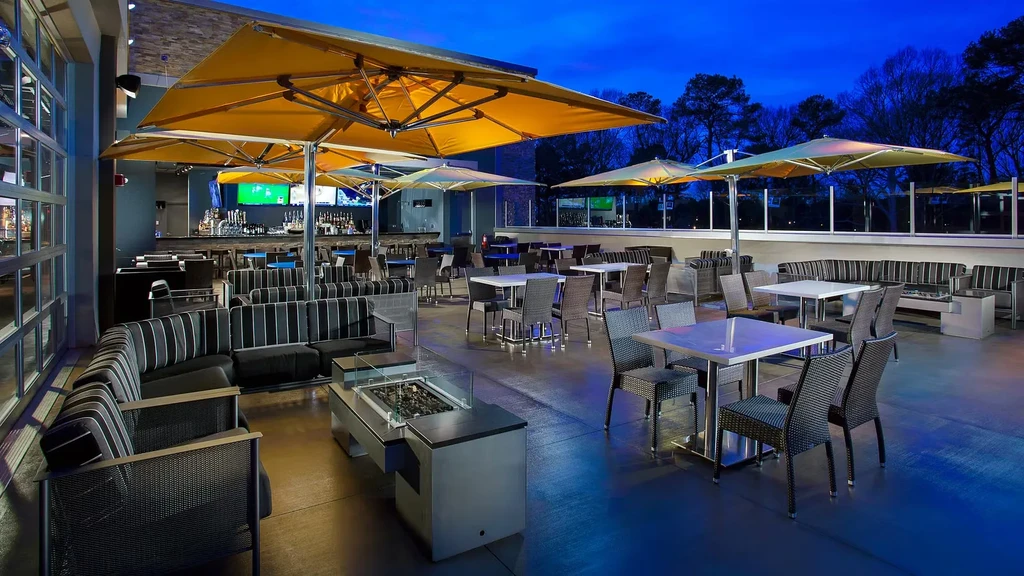 Modern outdoor restaurant patio at night with seating, fire pit, umbrellas.