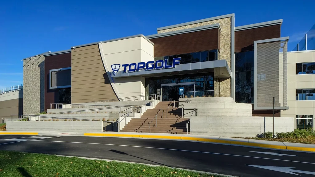 Modern Topgolf facility exterior with prominent logo under blue sky.