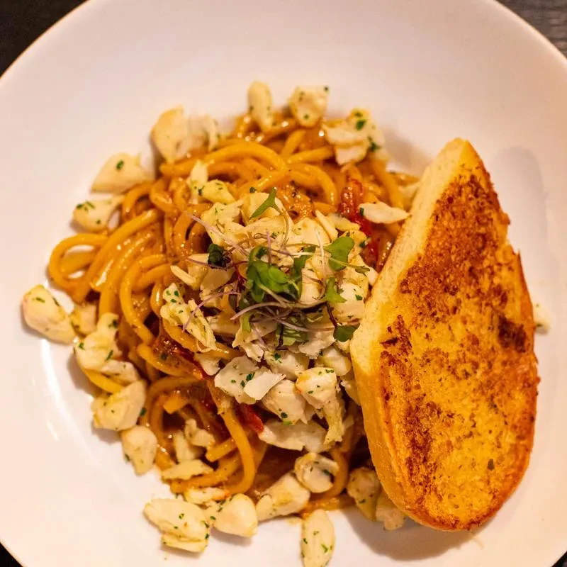 Close-up of spaghetti with crab, orange sauce, microgreens, and garlic bread.