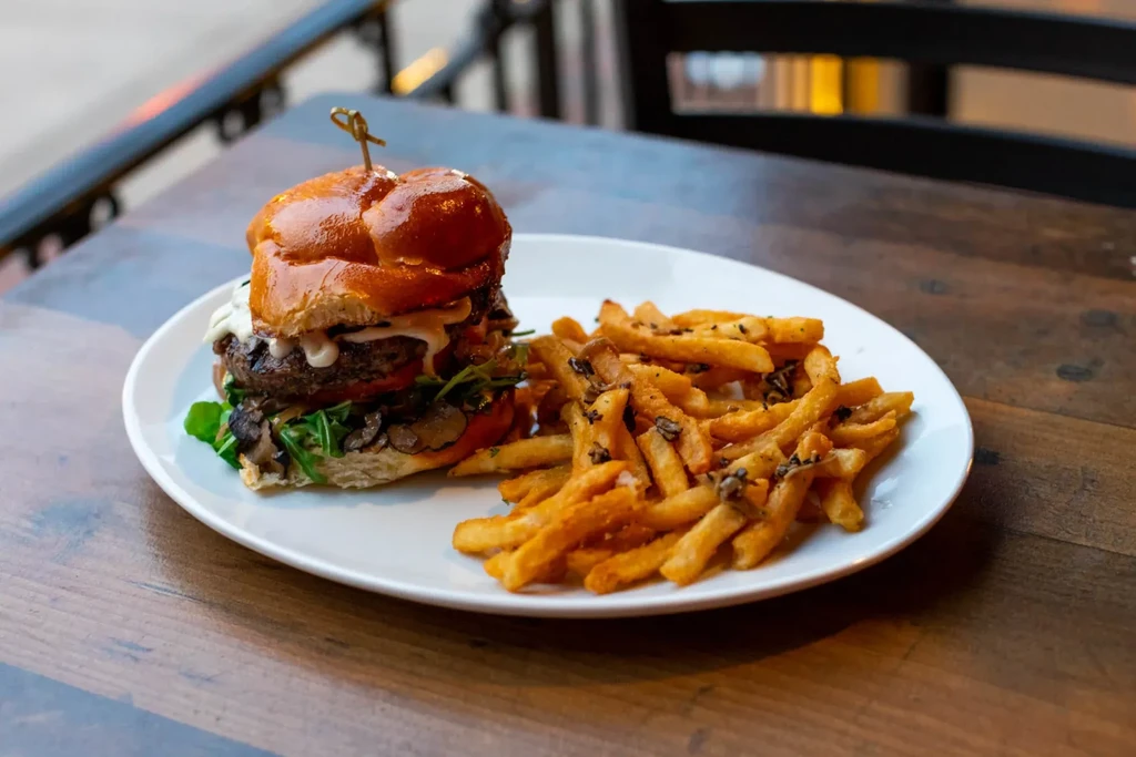 High-stacked gourmet burger with fries on a rustic wooden table.