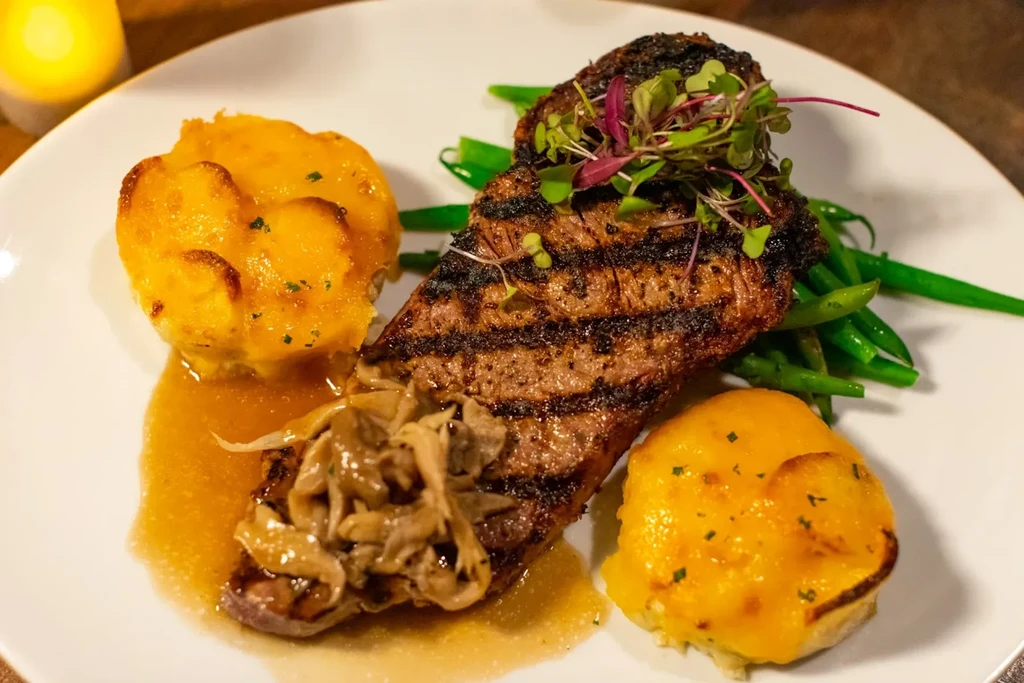 Grilled steak with char marks, microgreens, green beans, scalloped potatoes.