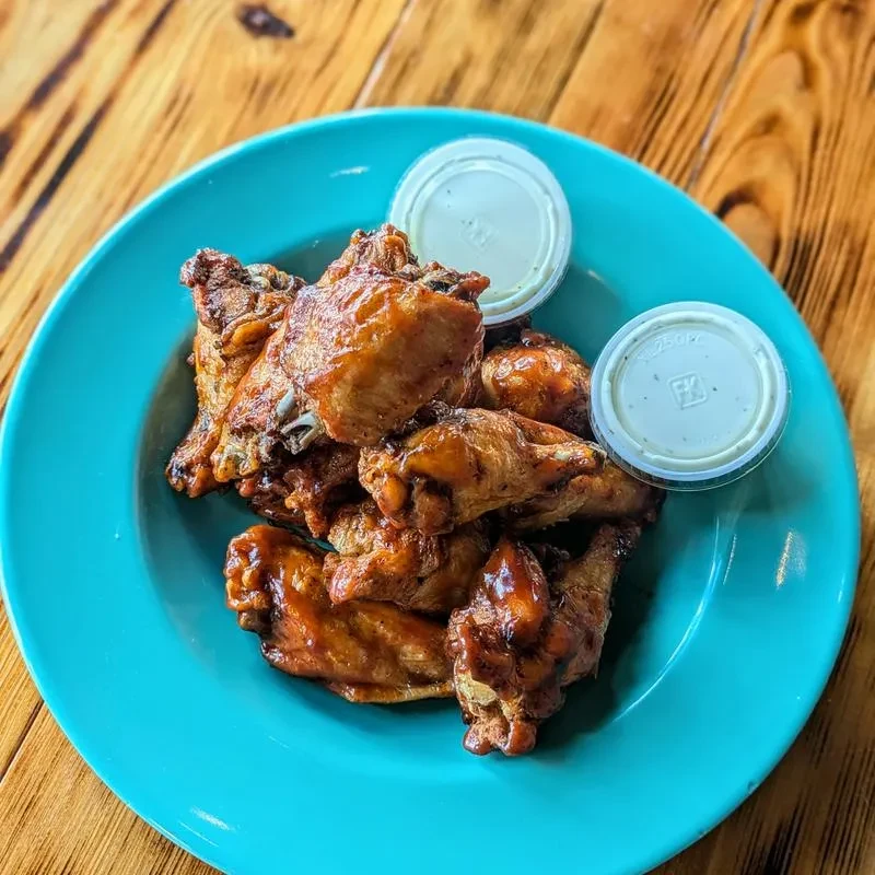 Glazed chicken wings on a blue plate with two dipping sauces.