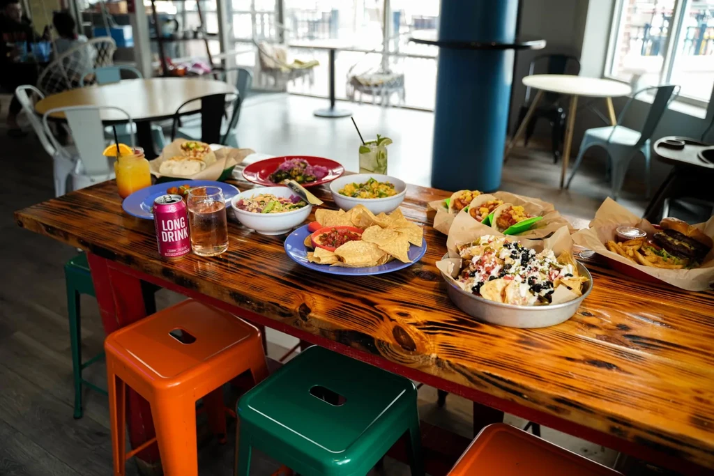 Vibrant food and drinks on a rustic communal table at a restaurant.