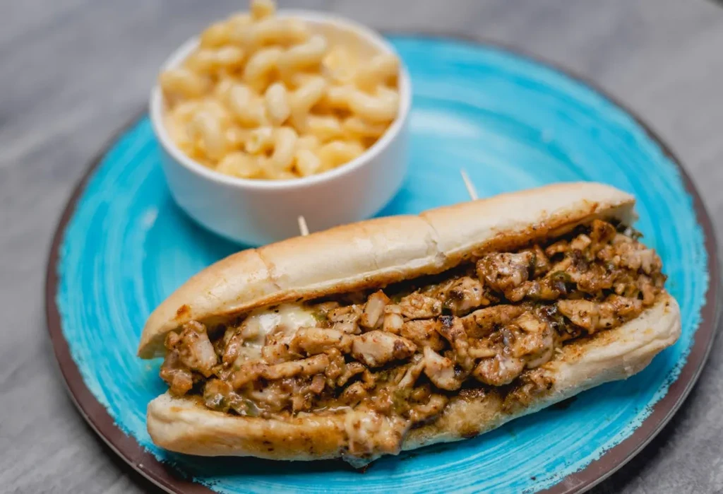 Chicken sub sandwich on blue plate with macaroni and cheese.