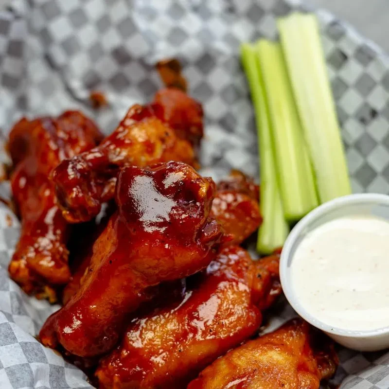 Glazed chicken wings, celery, and creamy dip served in a checkered basket.