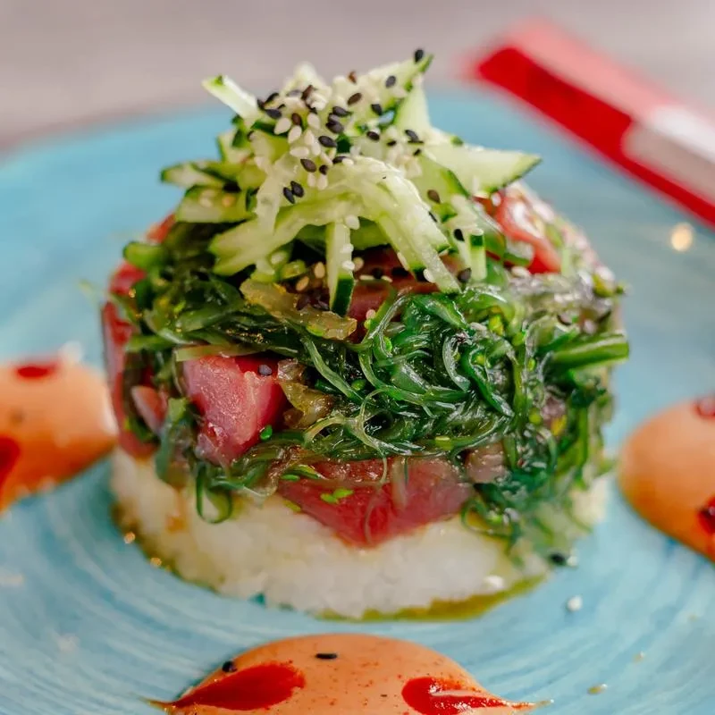 Stacked tuna poke, rice, green seaweed, orange sauce, blue plate.