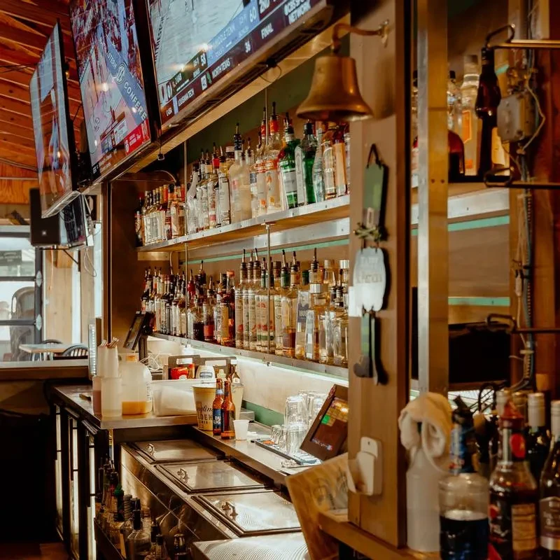 Well-stocked bar with liquor, TVs displaying sports, and a brass bell.