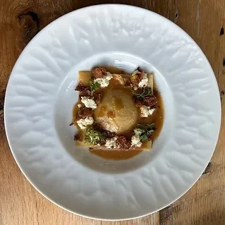 Meticulously plated pasta with brown sauce and fresh garnishes.