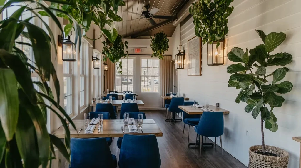 Bright, modern restaurant interior with blue chairs and abundant greenery.