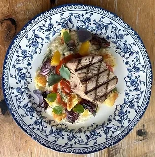 Grilled fish with risotto, colorful garnishes on an ornate blue-and-white plate.