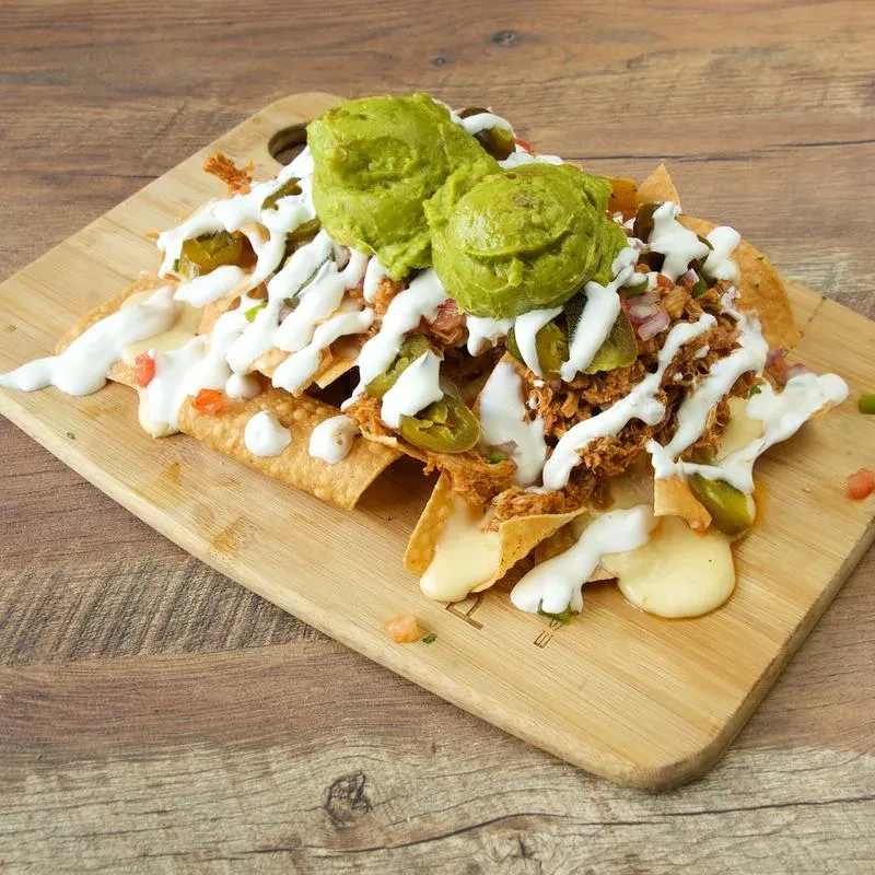Nachos with guacamole, shredded meat, jalapeños, cheese on a wooden board.