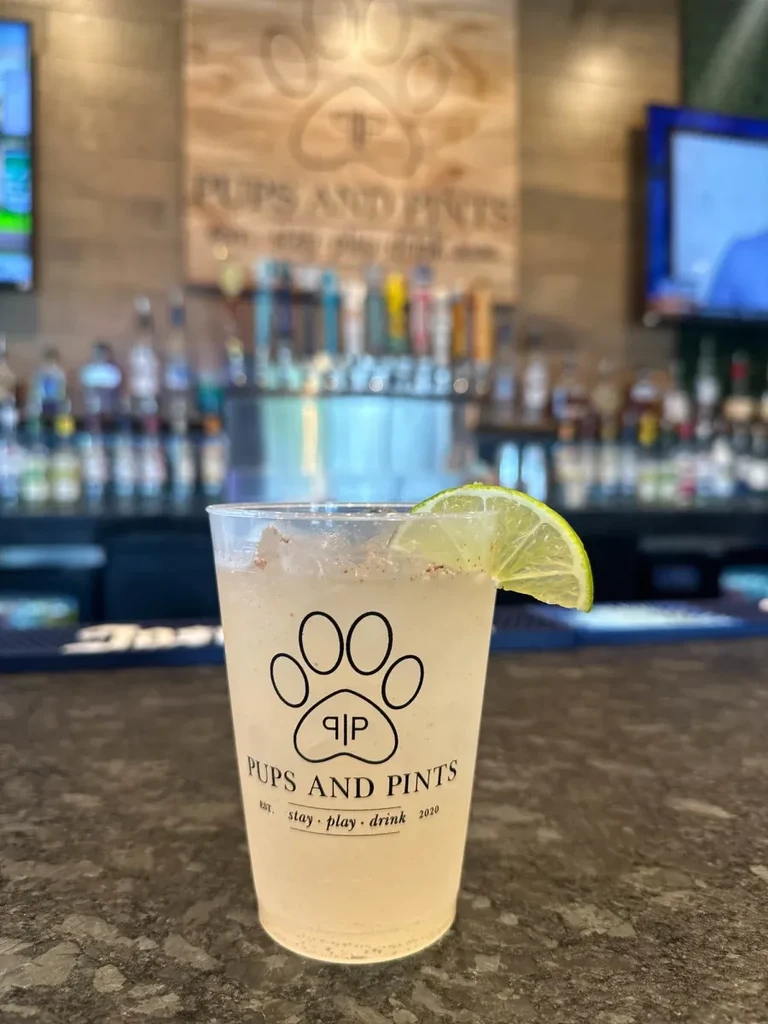 Iced drink with lime in a 'Pups and Pints' cup at a bar.