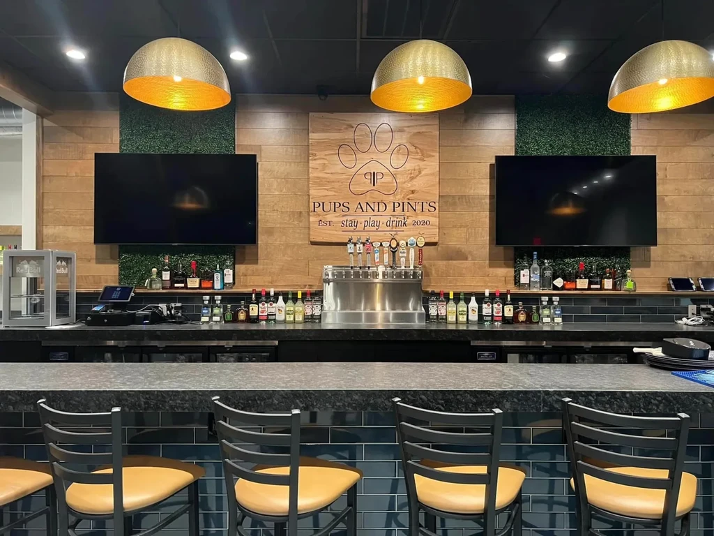 Modern bar with "Pups and Pints" sign, beer taps, and wood-grass walls.
